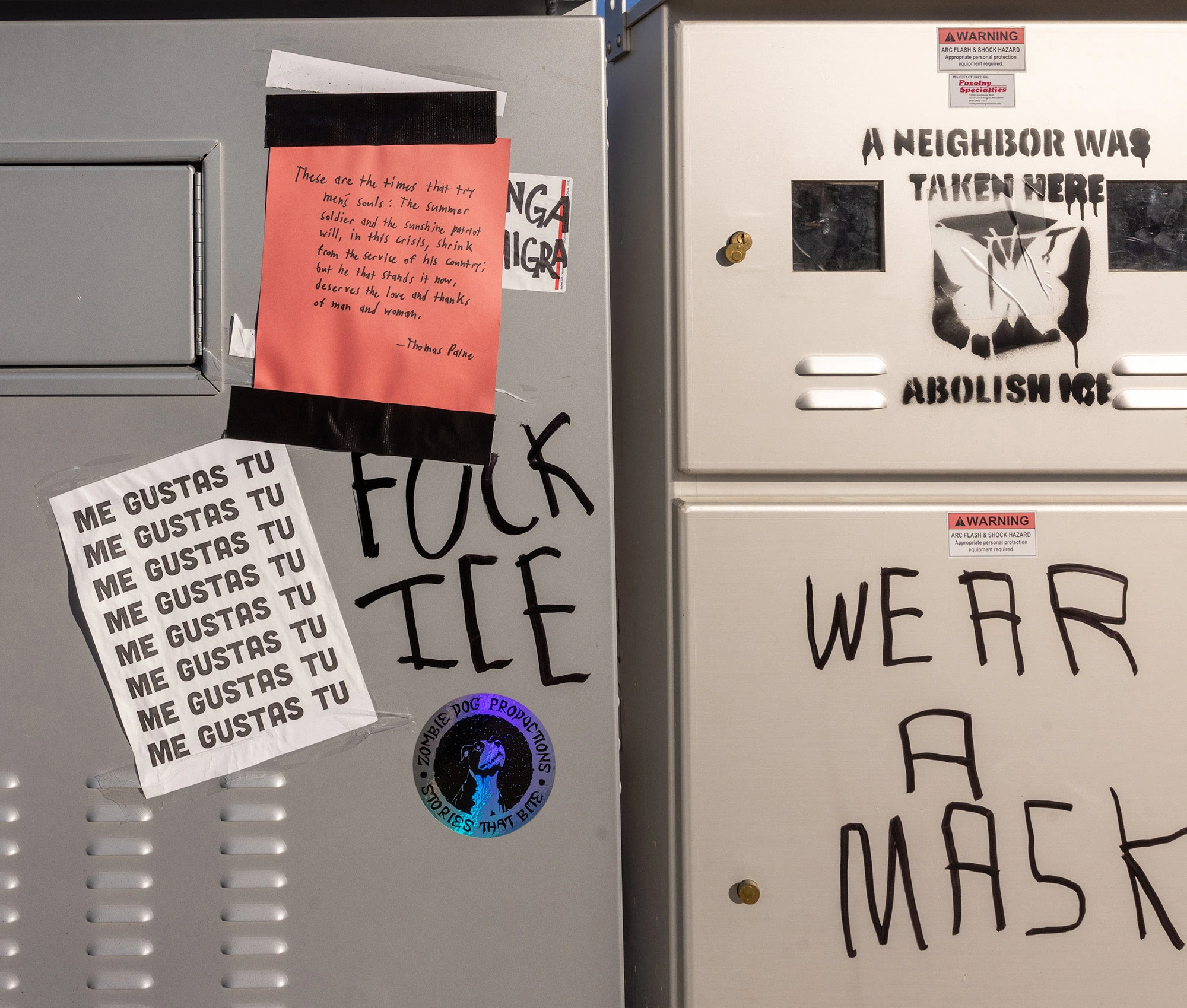 A cluster of stenciled and hand-written signs near the Renee Good memorial in Minneapolis, including messages reading 'A neighbor was taken here,' 'Abolish ICE,' and other protest slogans taped to utility boxes.