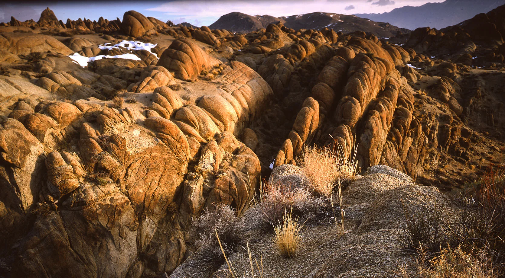 Weathered, rounded granite ridges of the Alabama Hills glowing at golden hour, snow patches and the Sierra beyond, Owens Valley