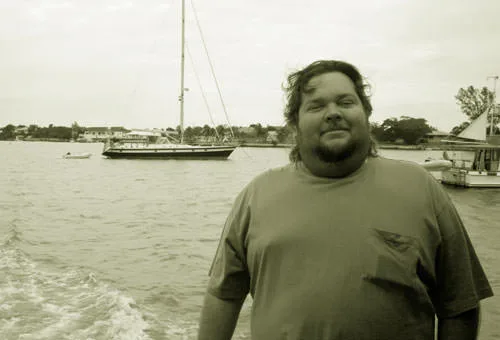Anthony, a bearded man in an olive shirt, aboard a boat off Great Guana Cay with sailboats behind