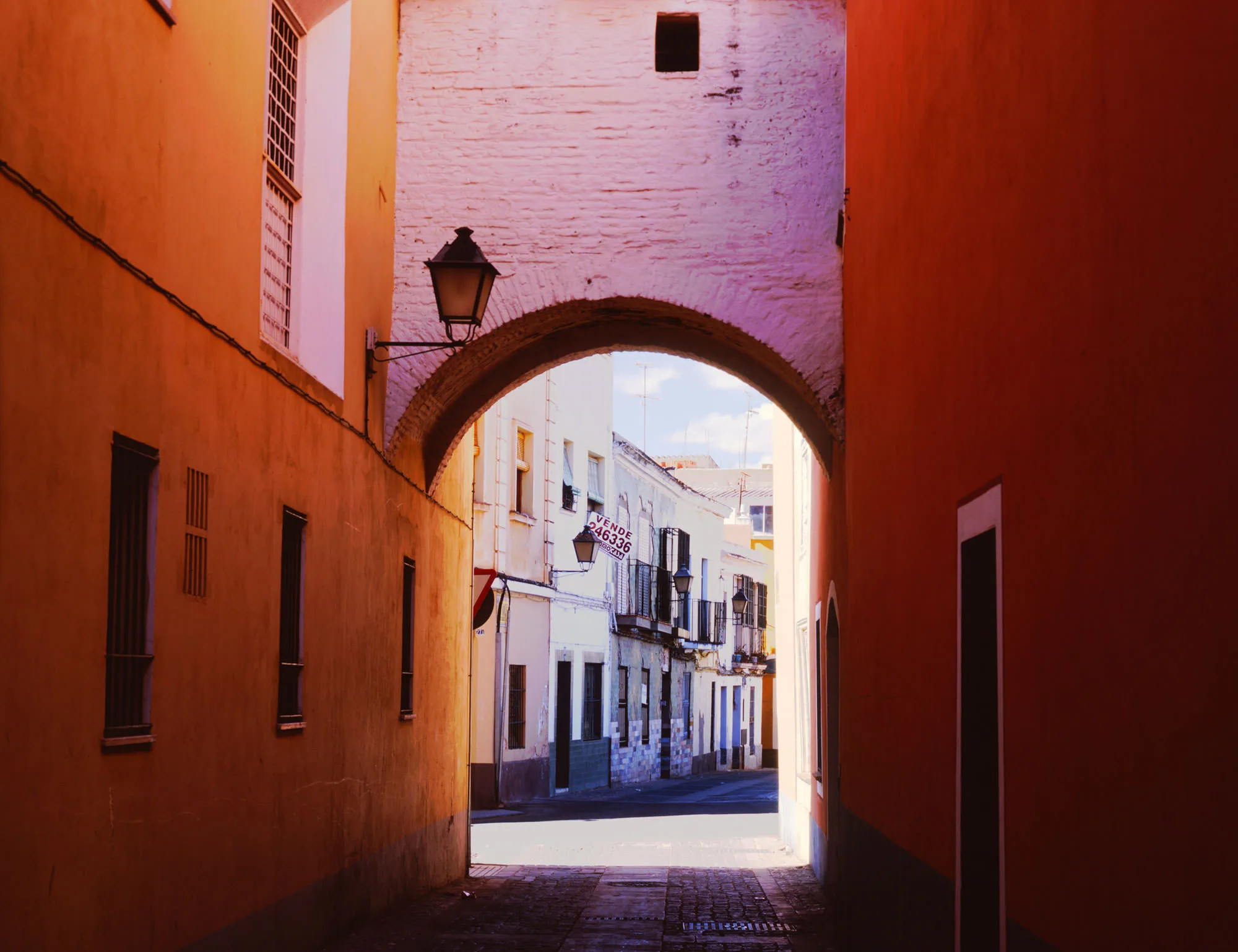 A sunlit brick archway framing a narrow street of orange-washed houses, Badajoz, Spain