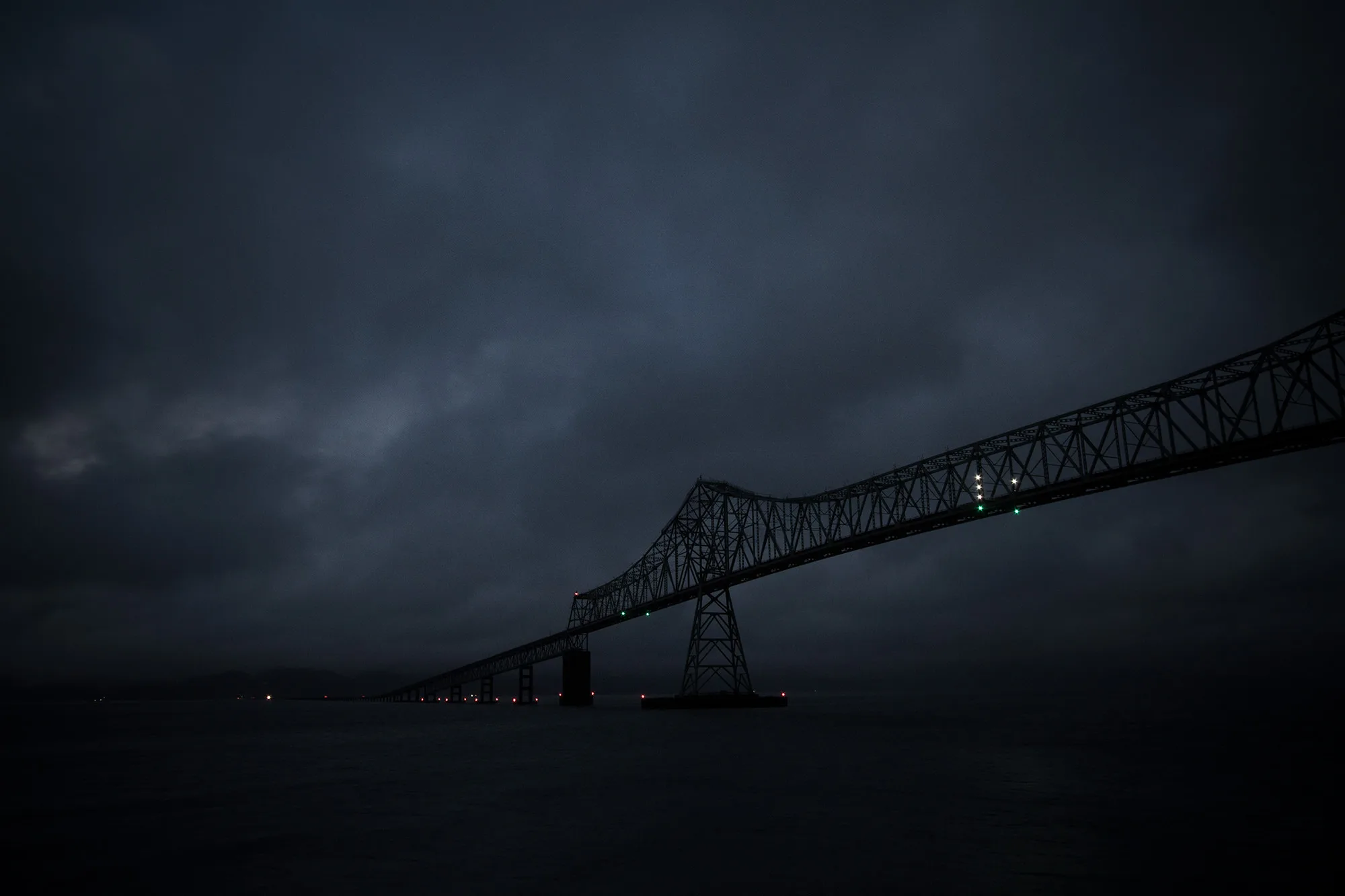 The Astoria-Megler Bridge silhouetted against a dark, stormy sky over the Columbia River.