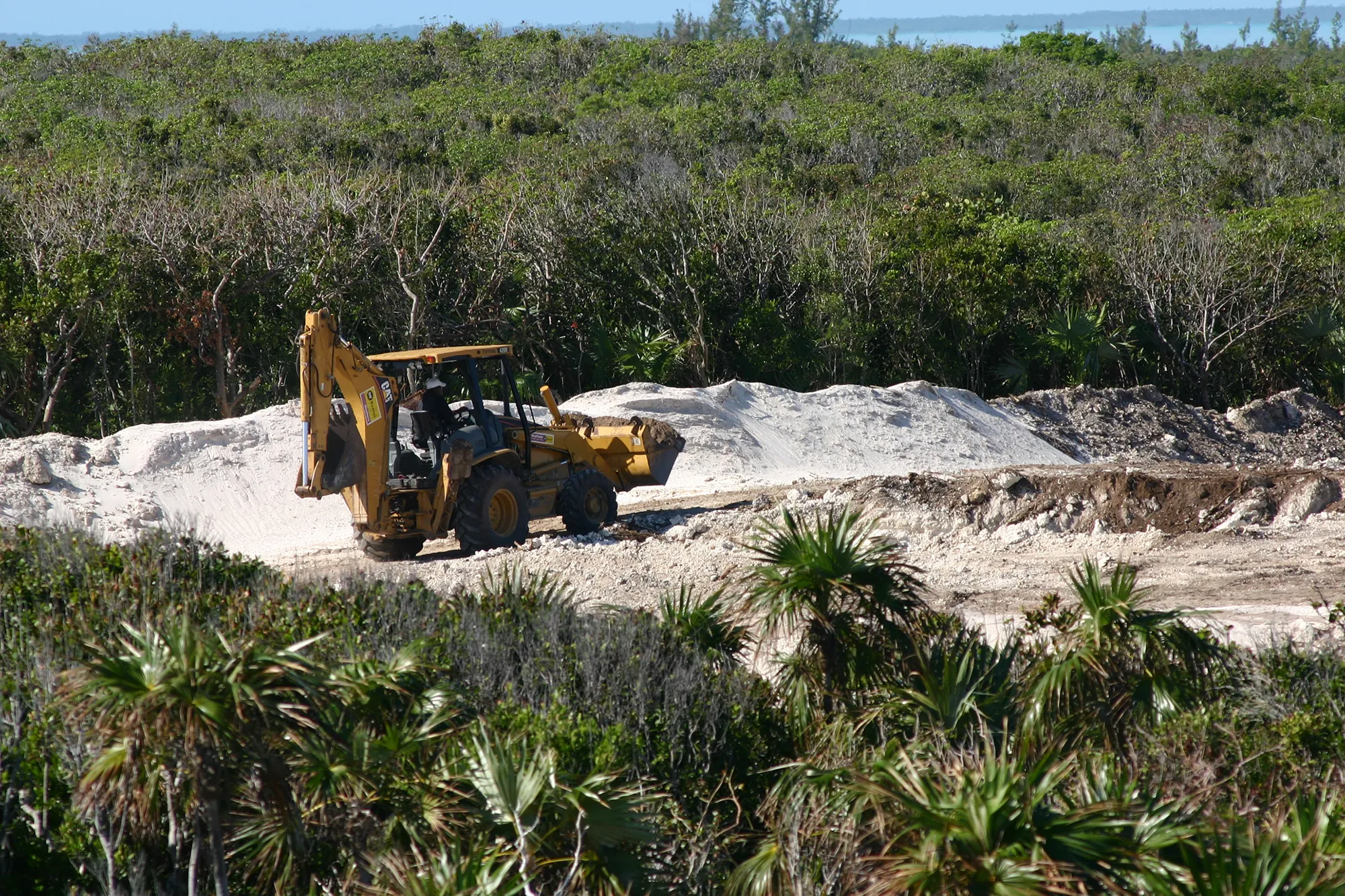 A backhoe working among piles of fill in cleared coppice forest at Bakers Bay, Great Guana Cay