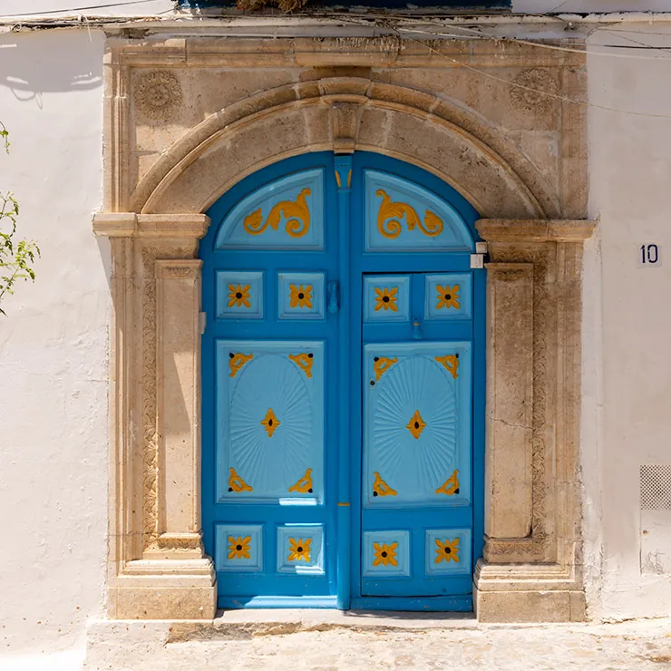 Blue arched door with yellow decorative patterns set in a carved stone frame in Sidi Bou Said, Tunisia.