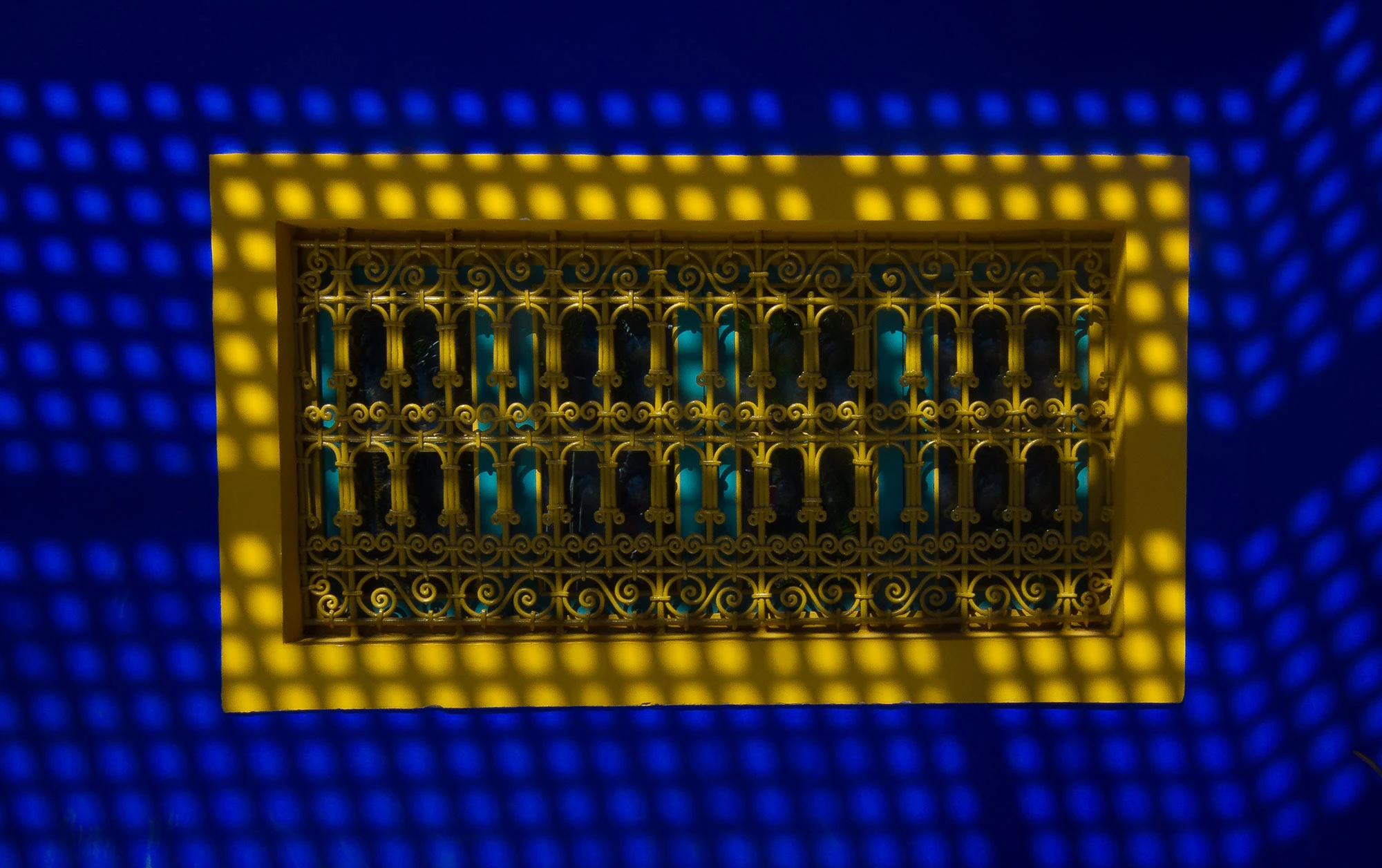 Sunlit lattice shadows falling across a yellow iron window frame in Marrakech's Majorelle Garden.