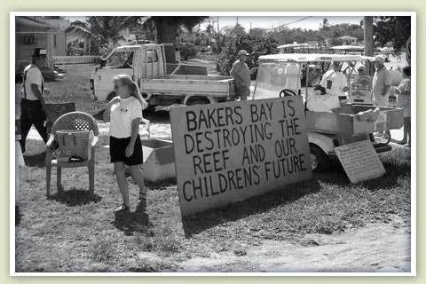 Black-and-white photo of Guana Cay residents beside a hand-painted sign reading "Bakers Bay is destroying the reef and our children's future."
