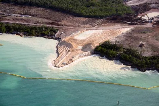 Aerial view of dredging sediment plumes spilling into turquoise water past a silt barrier at Baker's Bay