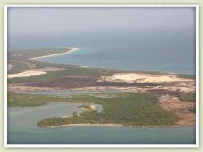 Aerial view of a low Bahamian island with mangrove creeks, cleared sand and a long beach.