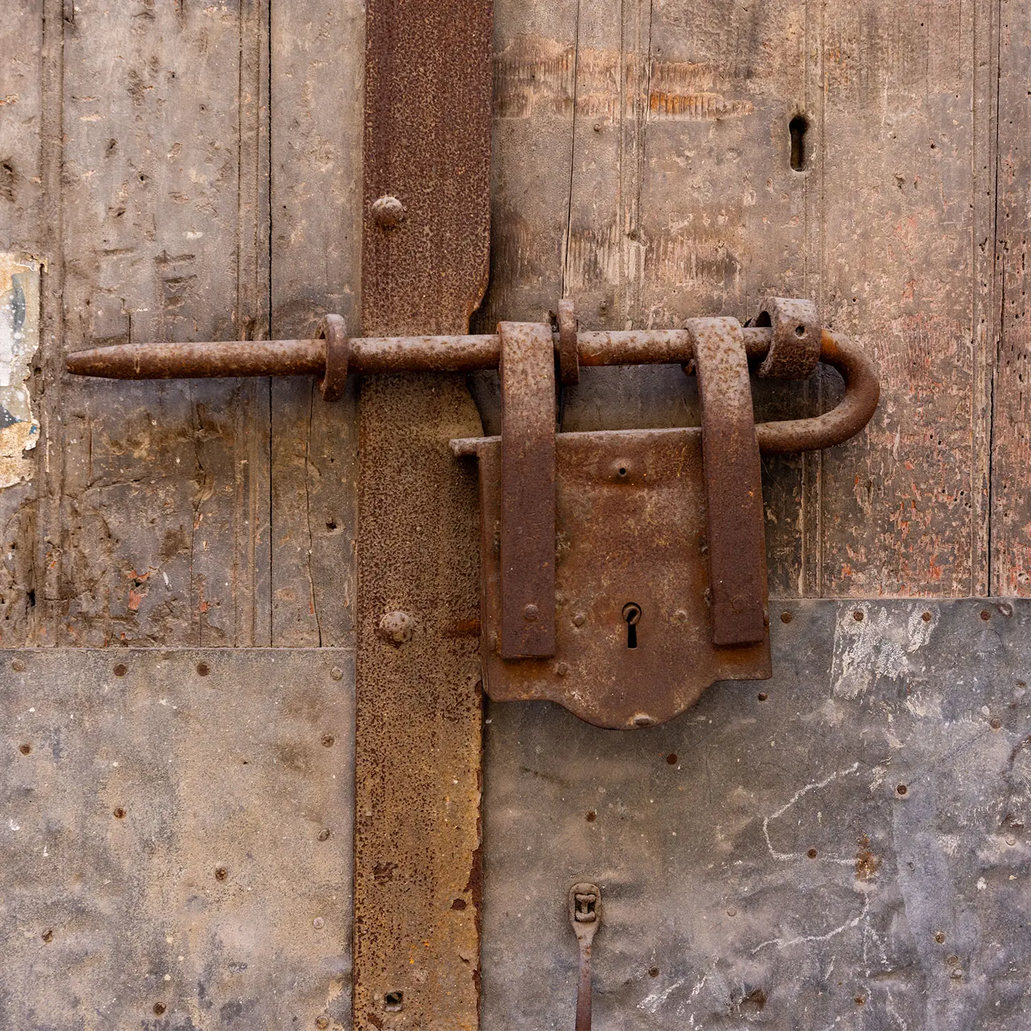 Rusted iron slide bolt and lock plate on a weathered, patched wooden door in Palermo, Sicily.