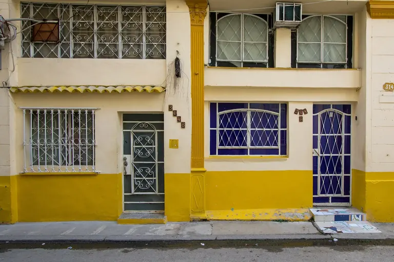 A yellow and white facade with blue doors and barred windows