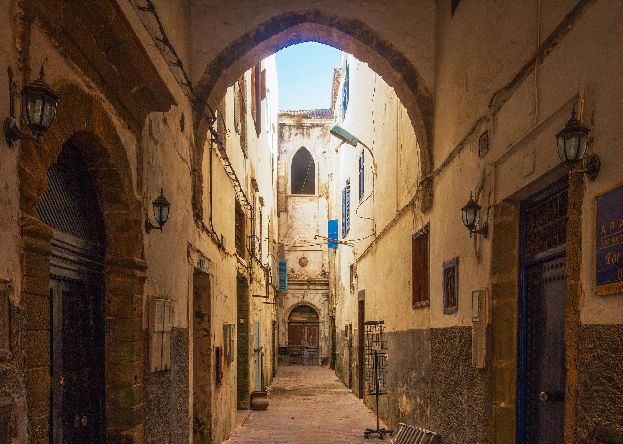 Stone arch framing a narrow alley with weathered walls and blue shutters in Essaouira's medina, Morocco