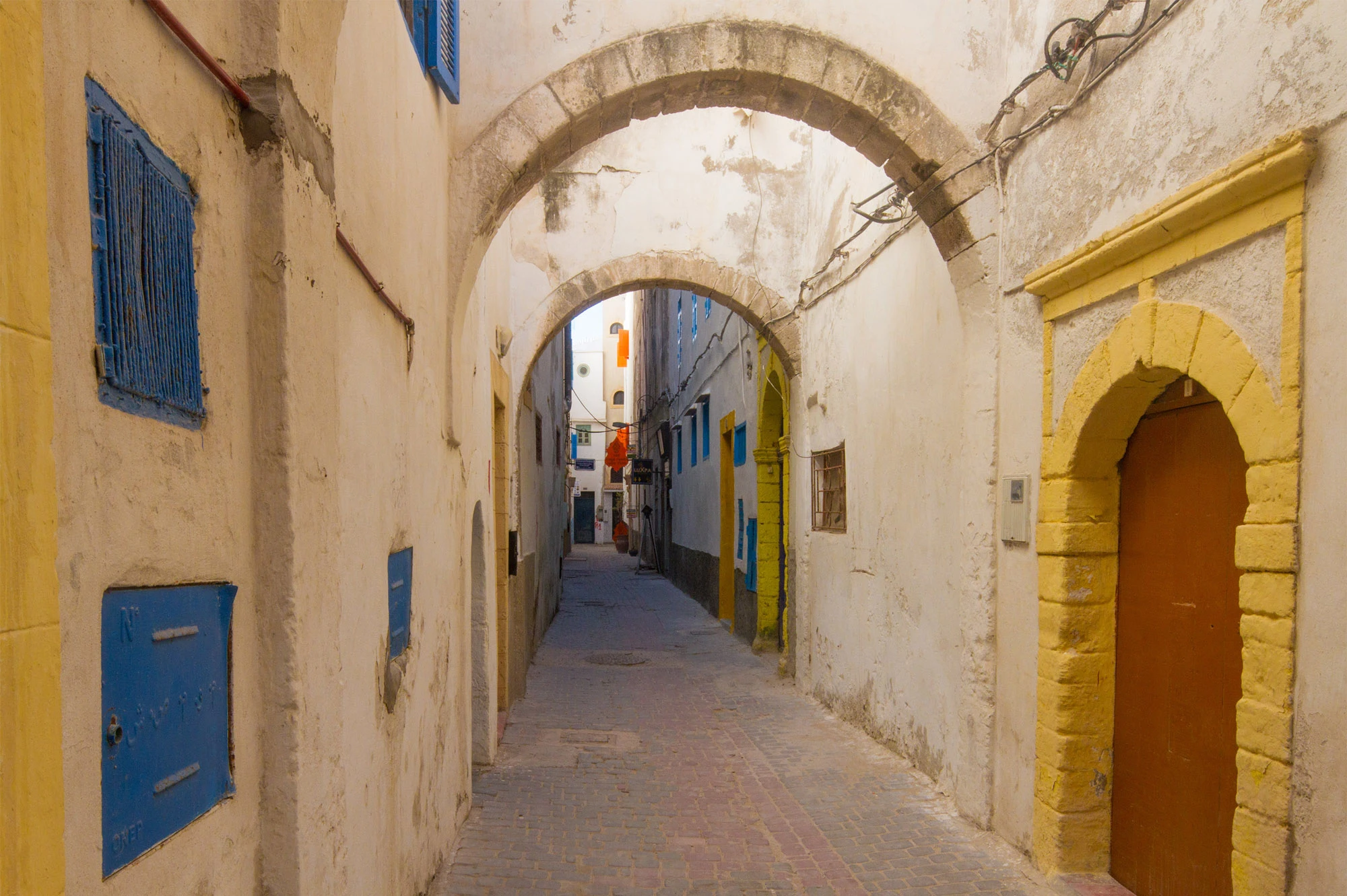 Narrow alley with stone arches and blue shutters in Essaouira's medina, Morocco