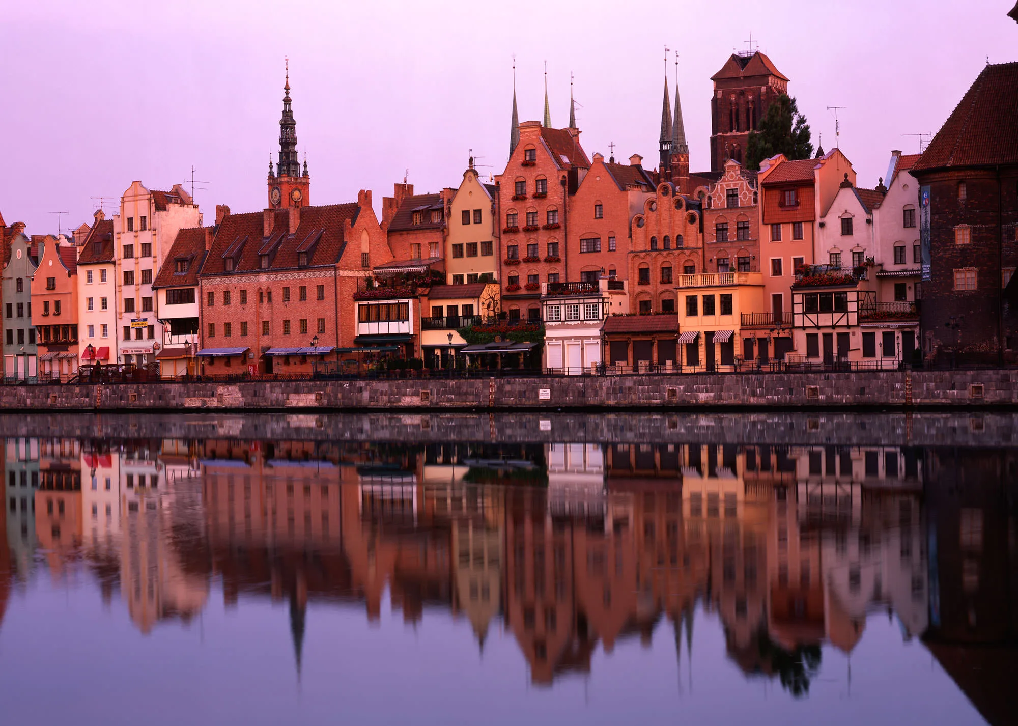 The gabled townhouses of Gdansk's old town glowing pink at dusk, reflected in the Motlawa River, Poland