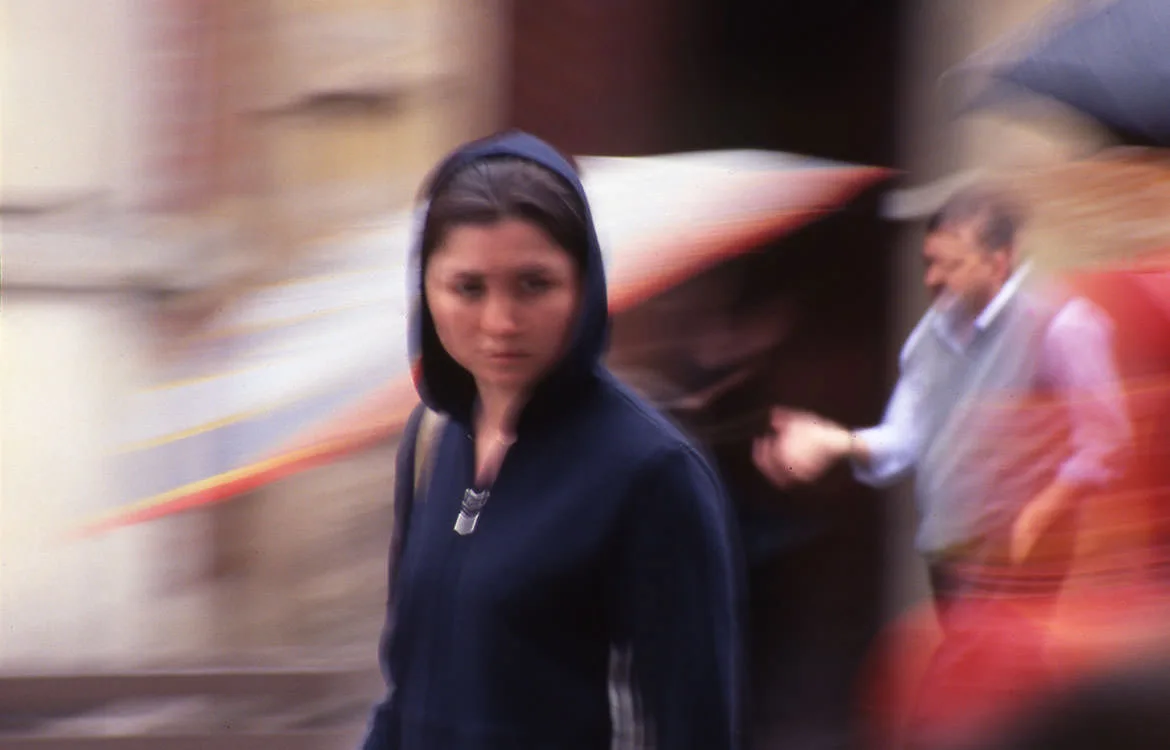 A motion-blurred street scene, a young woman in a hooded jacket passing through a Gdansk lane