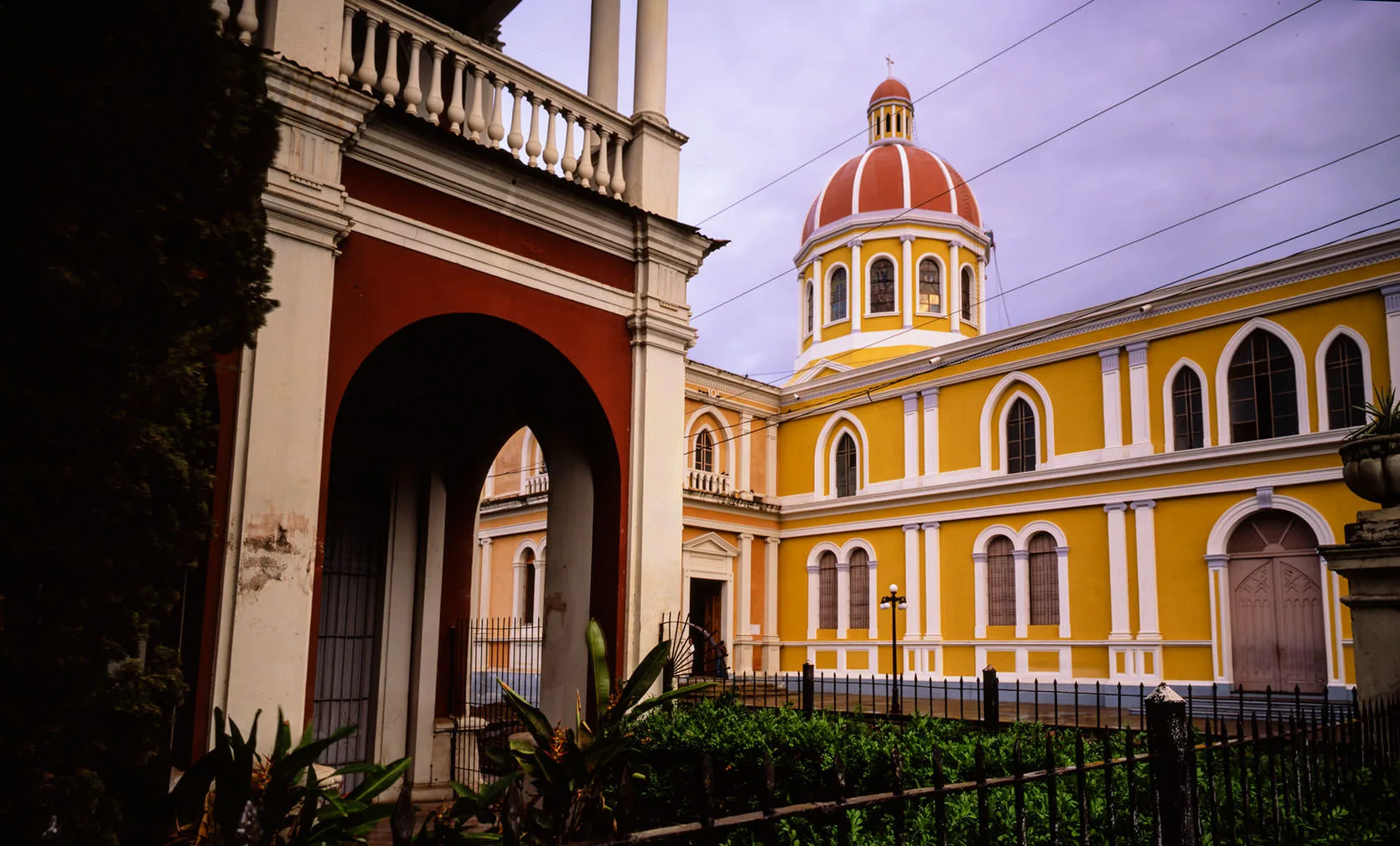Granada's yellow cathedral and red-tiled dome seen past a colonial white archway, Nicaragua