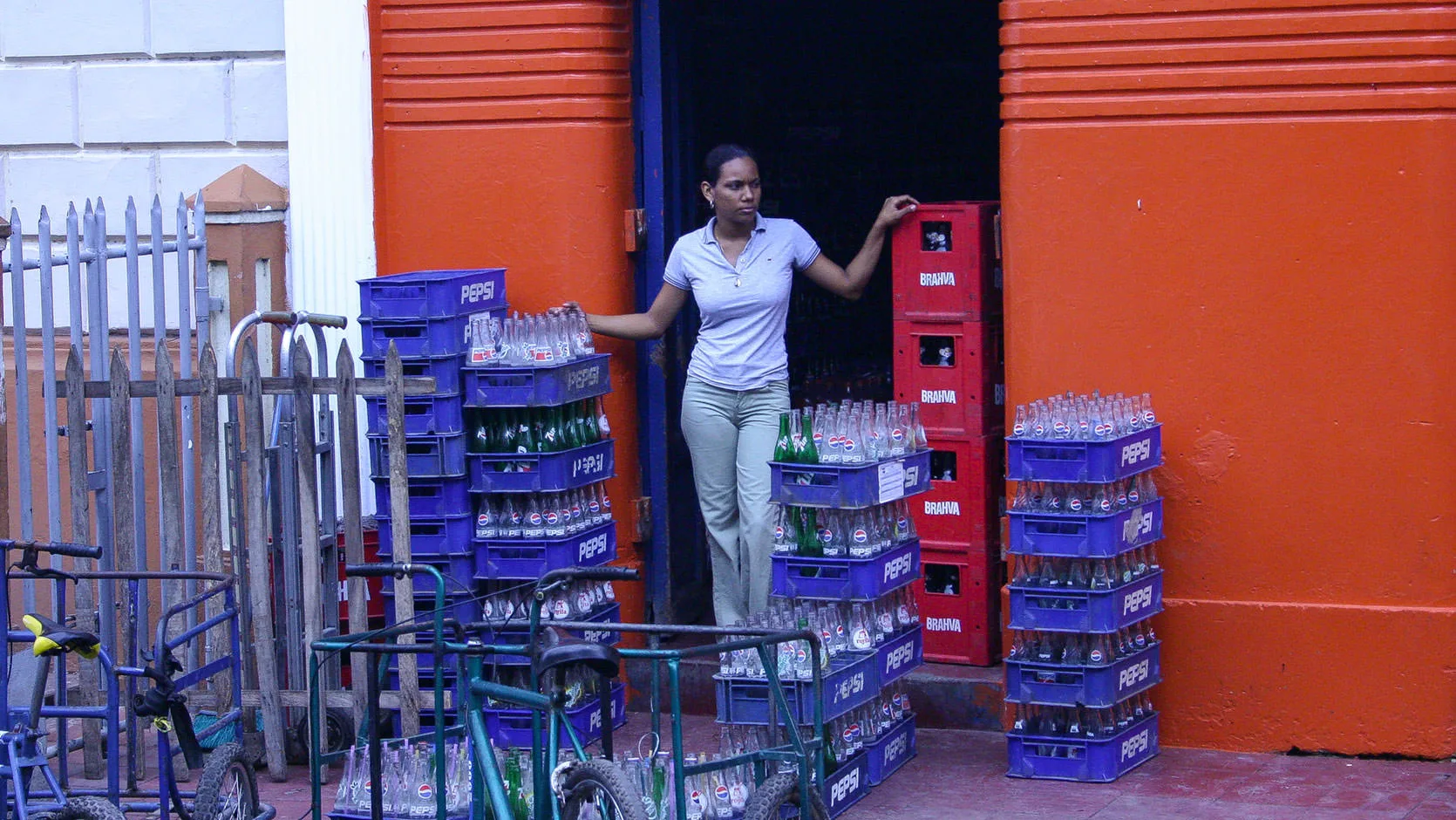 A young woman among stacked soda-bottle crates in the doorway of an orange shopfront, Granada