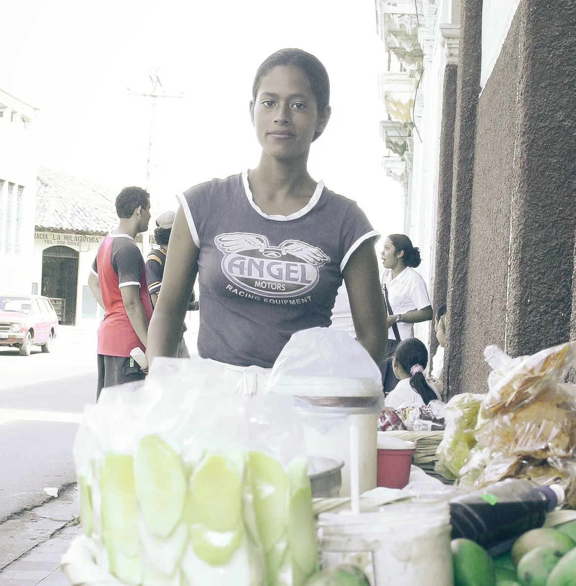 A young street vendor standing behind her cart of sliced green mango and snacks, Granada, Nicaragua