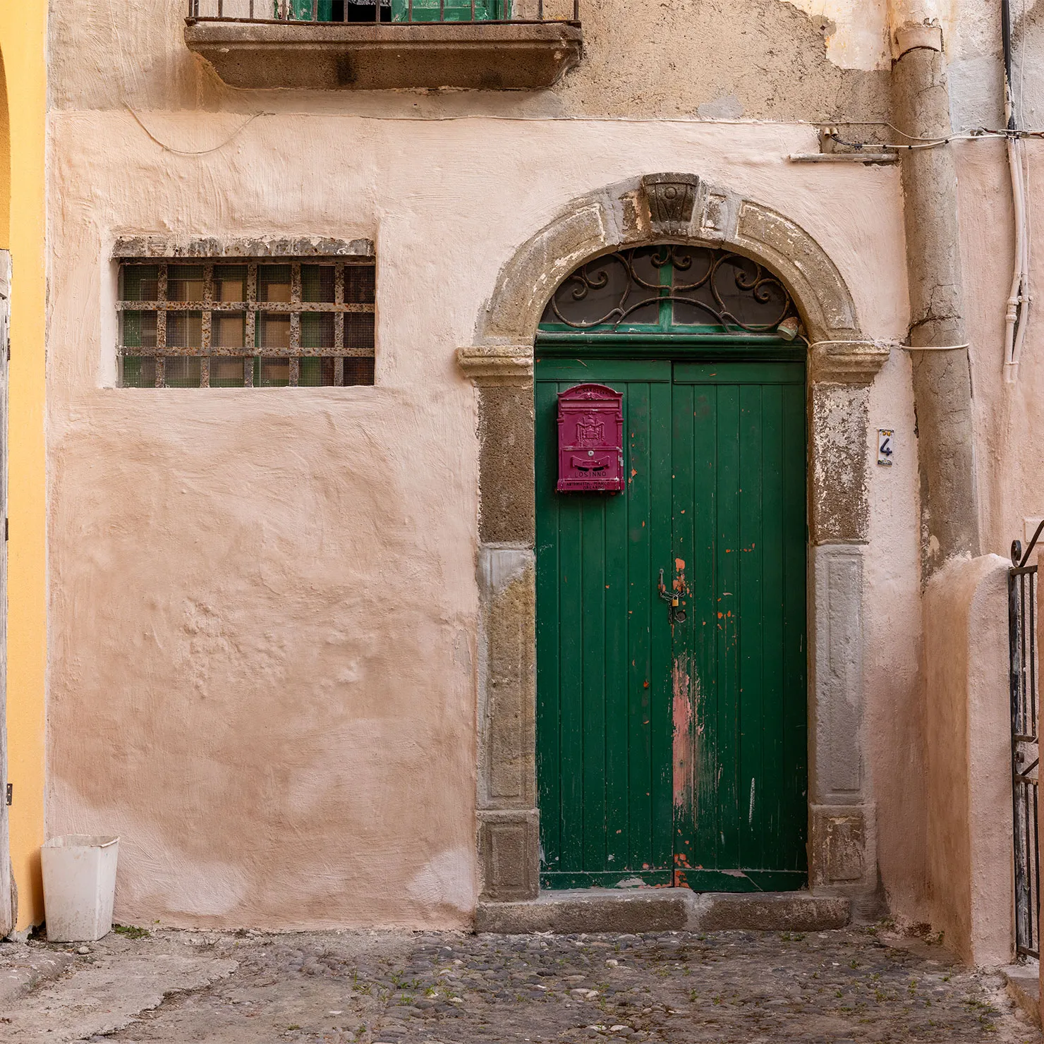 Green wooden door with a red mailbox beneath a stone arch in a pale plaster wall in Lipari, Aeolian Islands, Sicily.