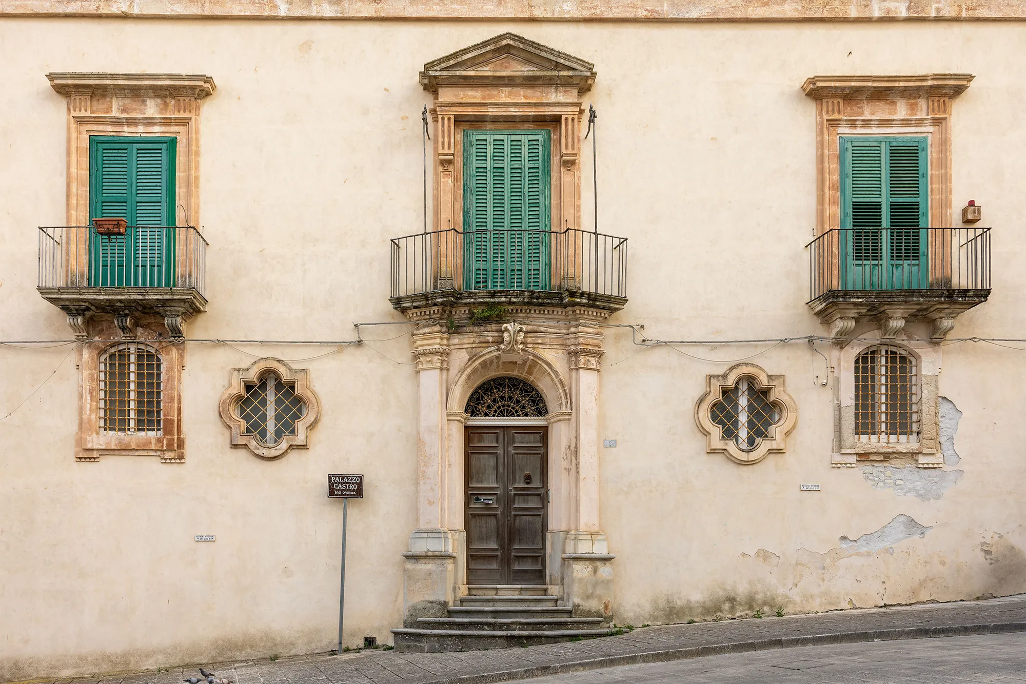 Palazzo Castro, a Baroque palazzo in Ragusa, Sicily, with green-shuttered windows over wrought-iron balconies, oval windows and an arched doorway.