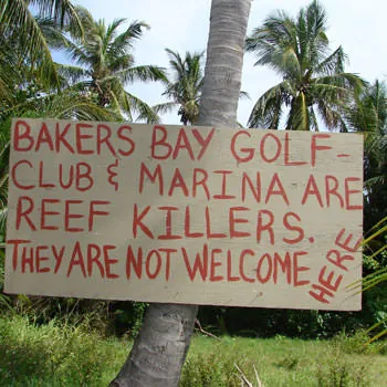 A hand-painted sign nailed to a palm reading "Bakers Bay Golf Club and Marina are reef killers. They are not welcome here."
