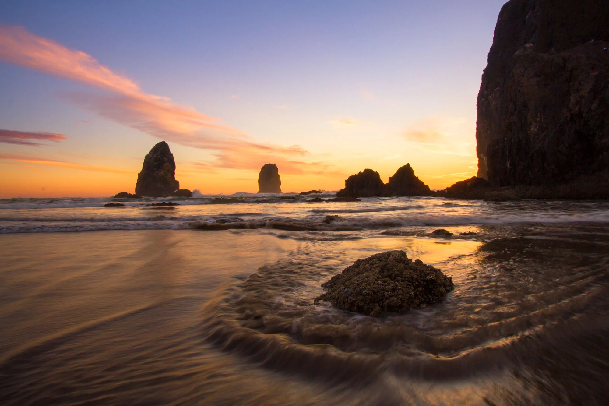 Sea stacks including Haystack Rock silhouetted against a soft sunset on the wet sand of the Oregon coast, Clatsop County