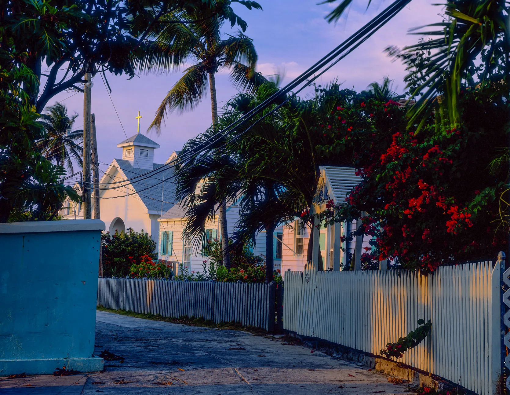 A white clapboard church with a steeple behind palms and a picket fence in Hope Town, Elbow Cay, Bahamas.
