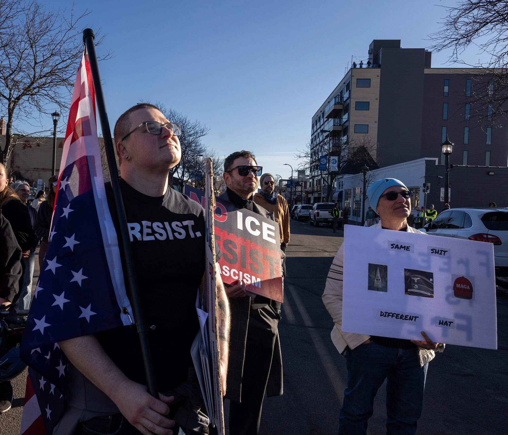 A group of demonstrators at the Alex Pretti memorial in Minneapolis standing with flags and protest signs.
