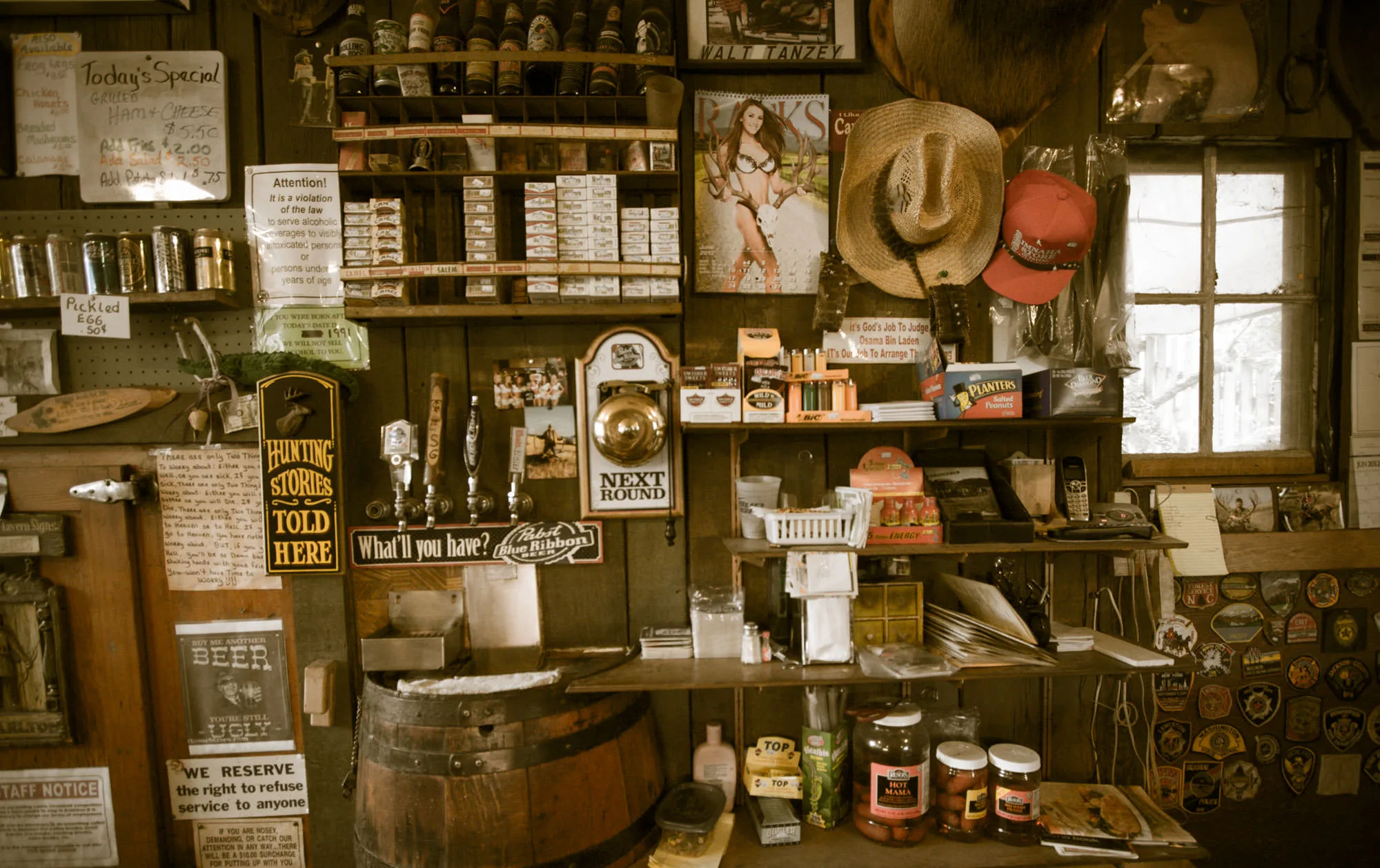 The cluttered interior of the Imnaha Tavern and Store, walls lined with hats, signs, bottles and old merchandise.