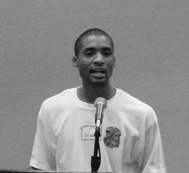 Black-and-white photo of Jermaine speaking into a microphone at a Save the Bahamas Coalition meeting.
