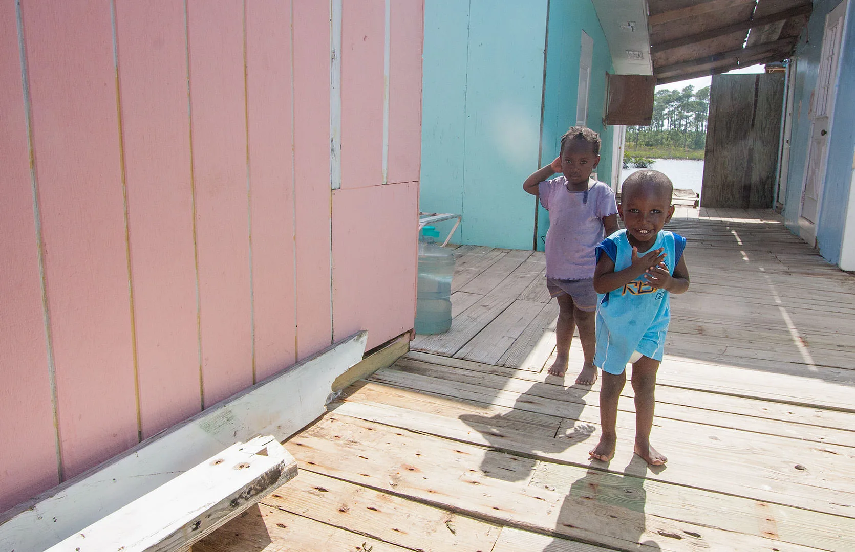 Two young children on the wooden walkway of a pastel shanty settlement, a Haitian community near Treasure Cay, Abaco