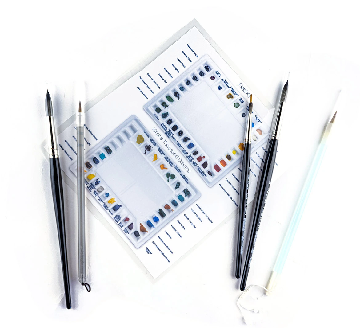 A laminated reference card made from a labeled overhead photograph of the studio watercolor palettes, naming the pigment in every well.