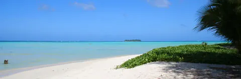White sand and turquoise water at Laolao Bay, Saipan, with a small island on the horizon.