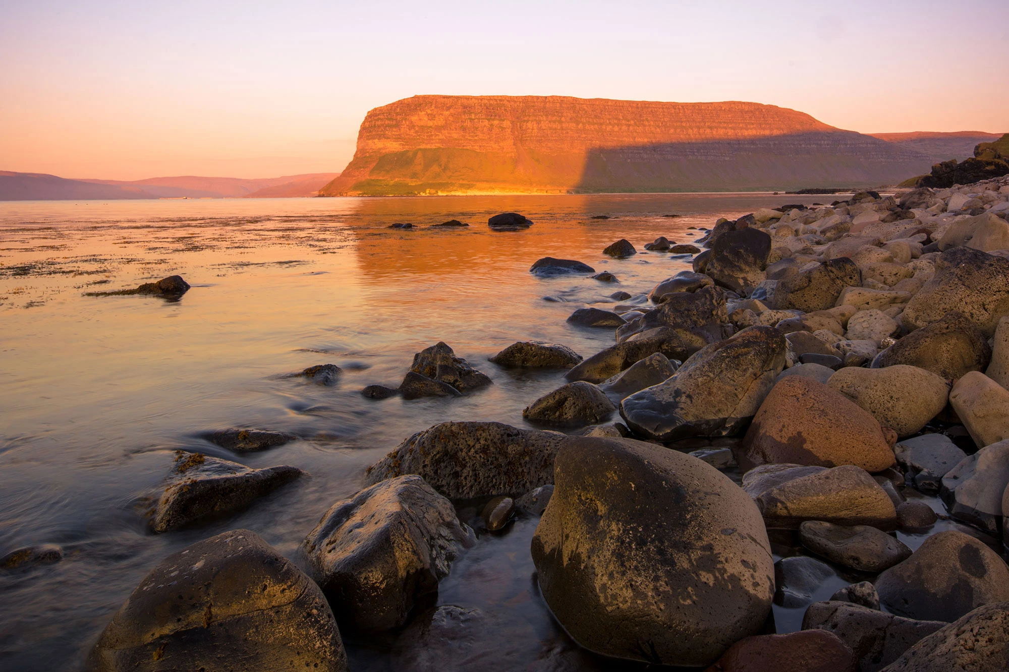 Sunset over Patreksfjörður fjord near Látrabjarg in Iceland's Westfjords, where the quiet fishing town glows in midnight light beneath pastel skies reflected in the still waters.