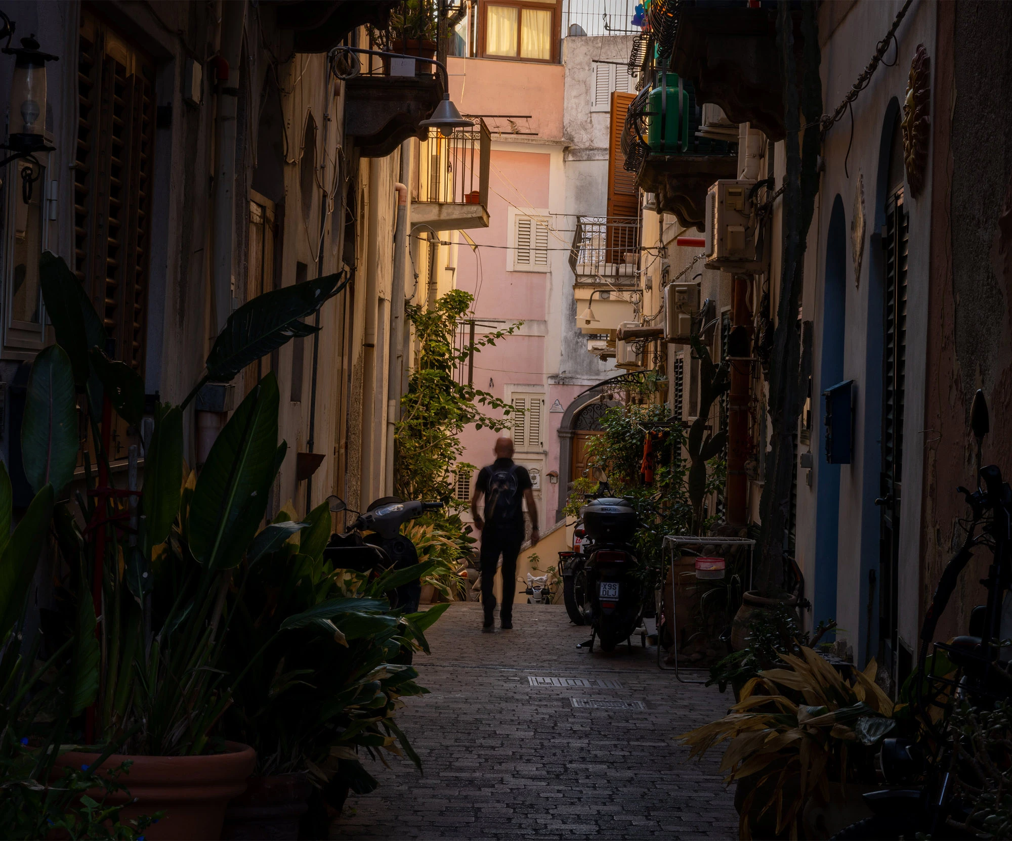 A narrow, sunlit alley in Lipari town, Aeolian Islands, hung with plants and washing.