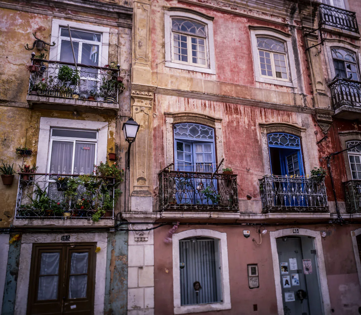 Weathered pastel facades with plant-filled iron balconies and a street lamp in the Alfama, Lisbon