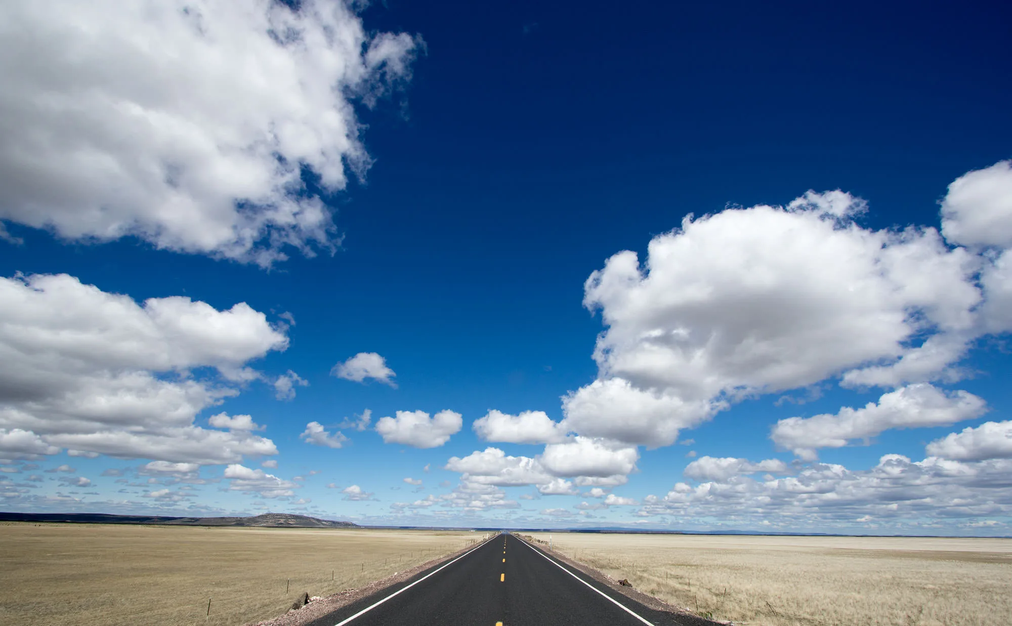 A straight, empty highway running to the horizon under a big sky of cumulus clouds across the high desert, Malheur
