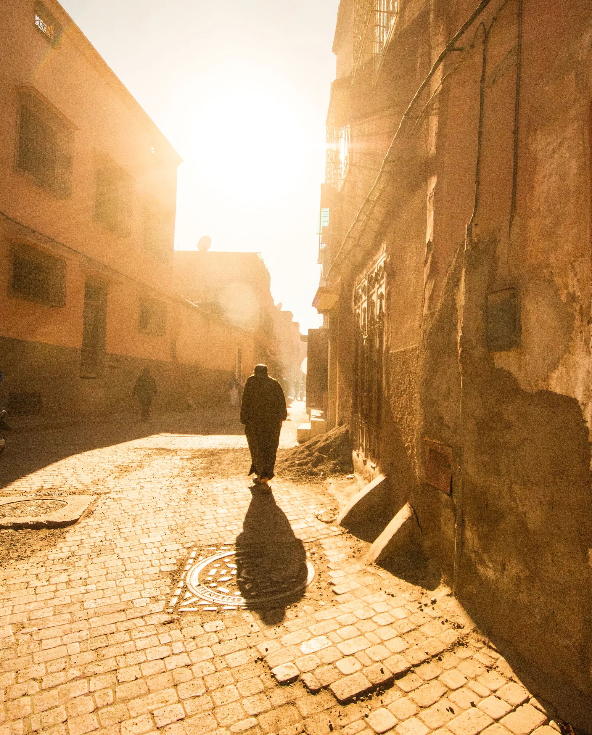A man walking through a sun-drenched alley in Marrakech, his shadow stretching across the cobblestones.