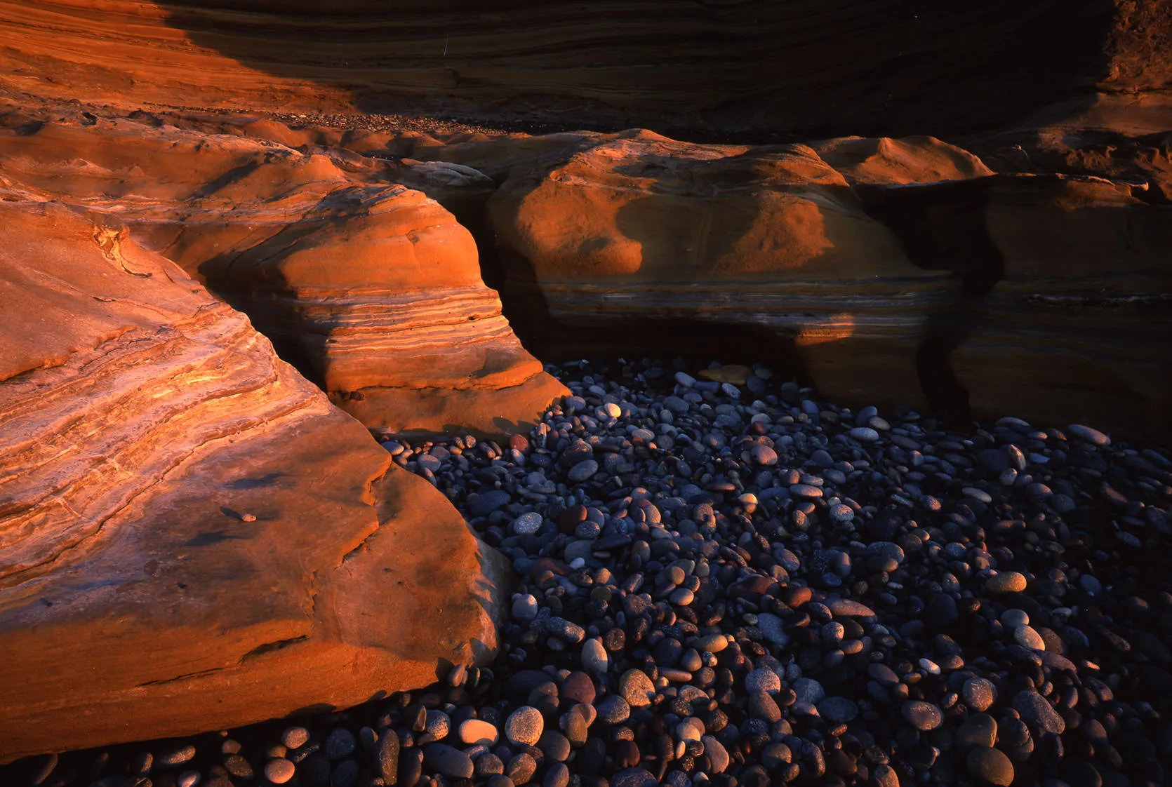 Smooth layered sandstone boulders glowing orange above a beach of dark round cobbles on Baja's Pacific coast.