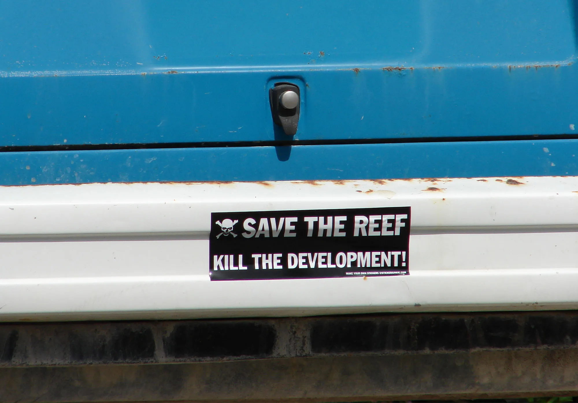 “Save the Reef, Kill the Development!” bumper sticker on a weathered blue truck on Great Guana Cay
