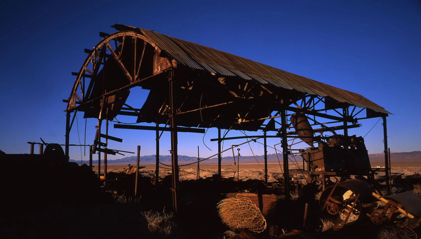 The rusted frame and wheel of an abandoned mine structure outside Rachel, Nevada, against a deep blue sky.