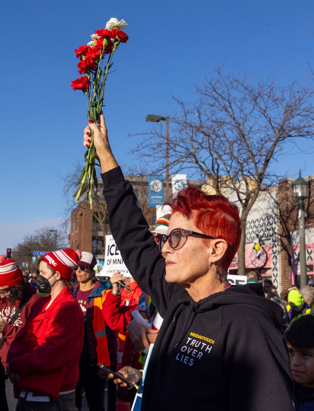 A woman holds red carnations high above a vigil crowd