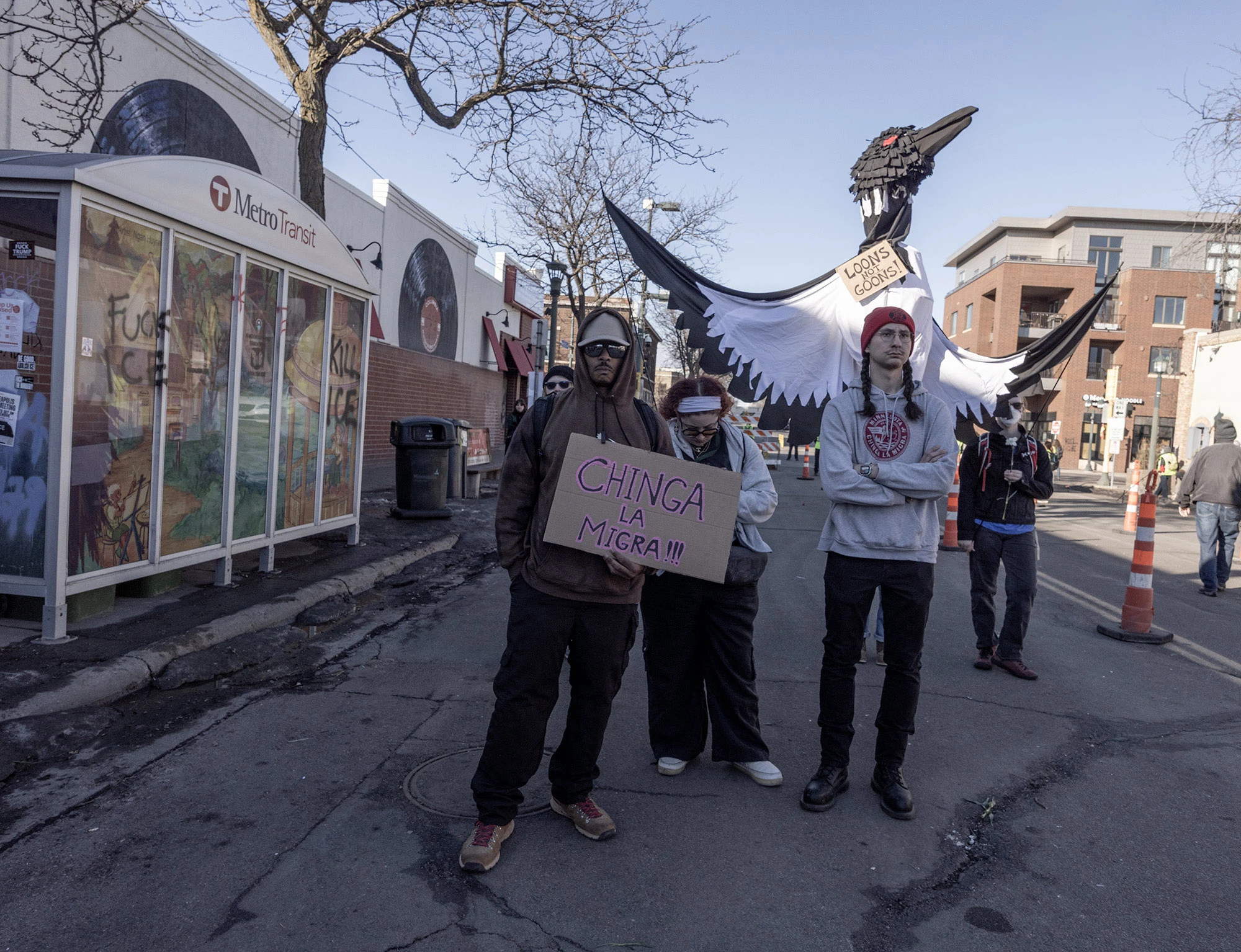Protesters stand in a Minneapolis street beneath a towering black-and-white loon puppet bearing the phrase 'Loons Not Goons' during demonstrations following the fatal shooting of Alex Pretti.