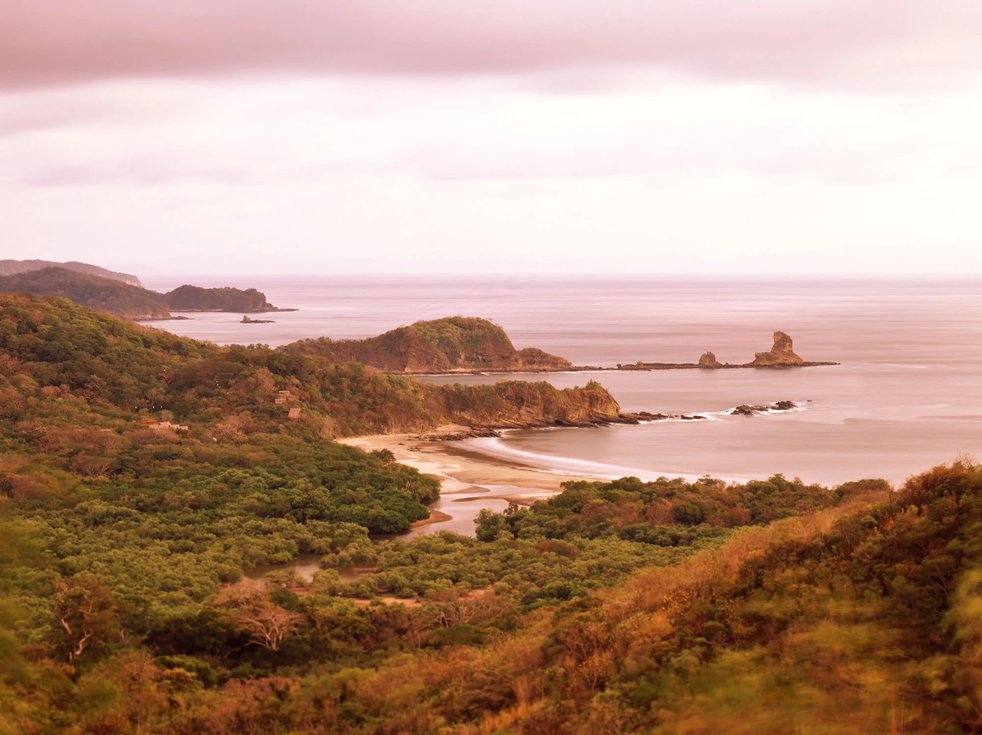 A forested Pacific coastline with a curving beach, estuary and sea stacks at dusk, Morgan's Rock, Nicaragua