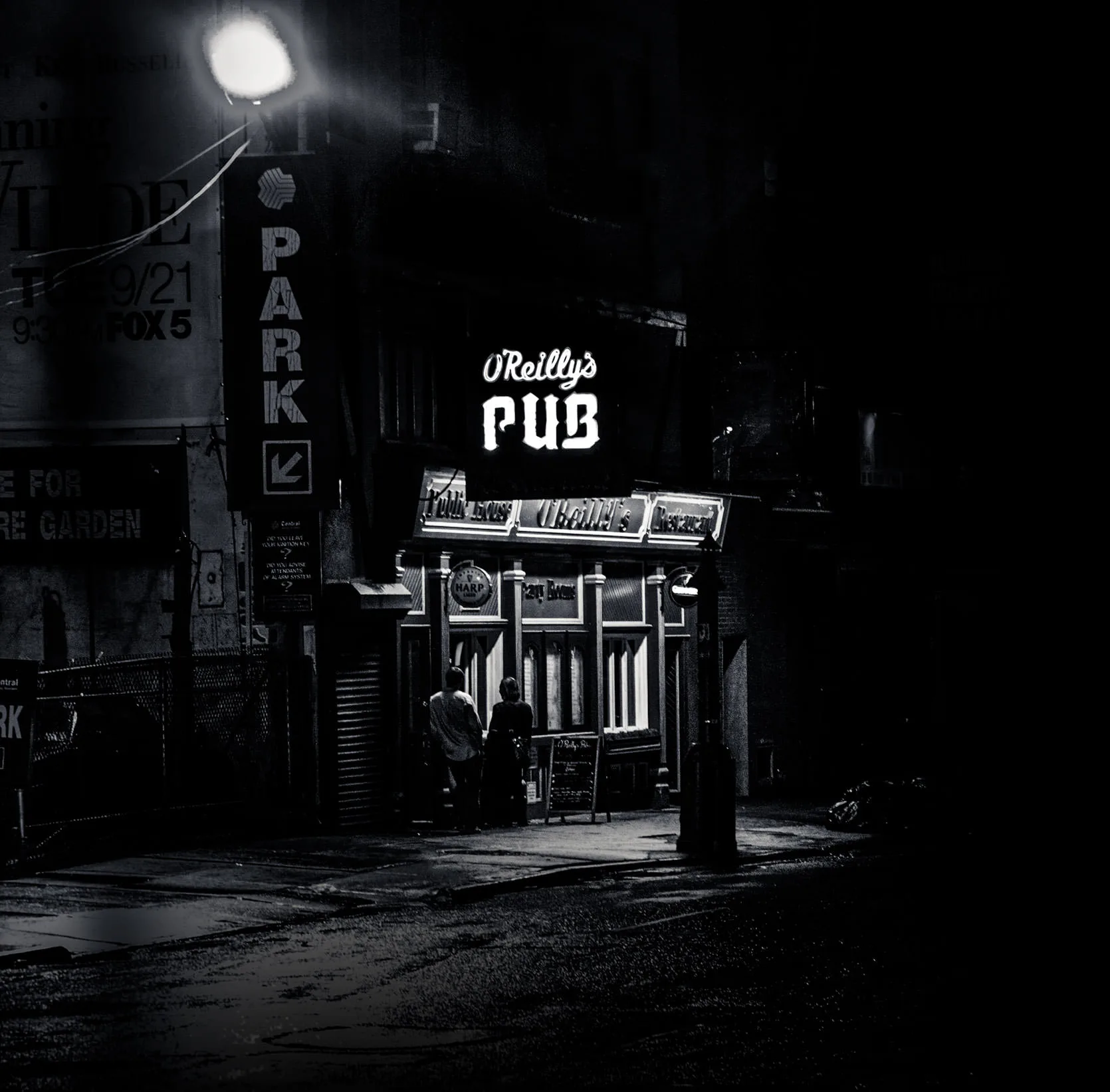 Black-and-white photo of the glowing O'Reilly's Pub sign on a dark New York street at night.