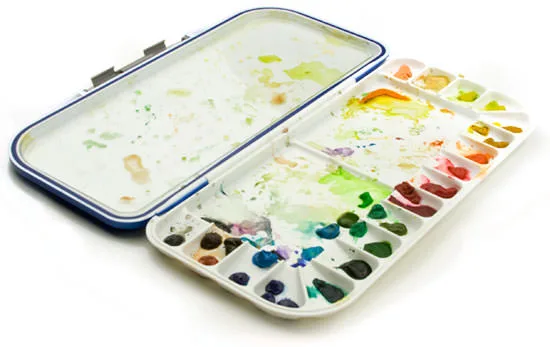 An open waterproof travel watercolor palette with well-used paints and a mixing area.