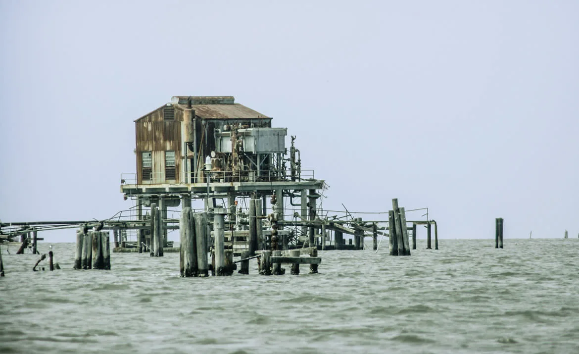 A rusted, abandoned industrial platform standing on pilings in open Gulf water, Port Sulphur, Louisiana