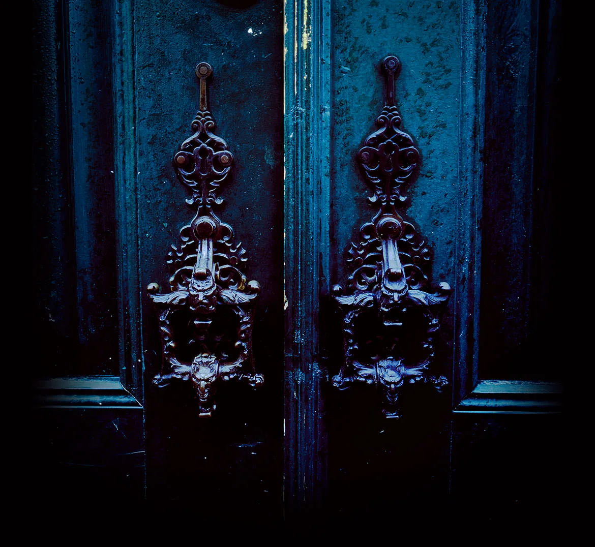 Ornate antique iron knockers on a weathered blue double door, Alfama, Lisbon