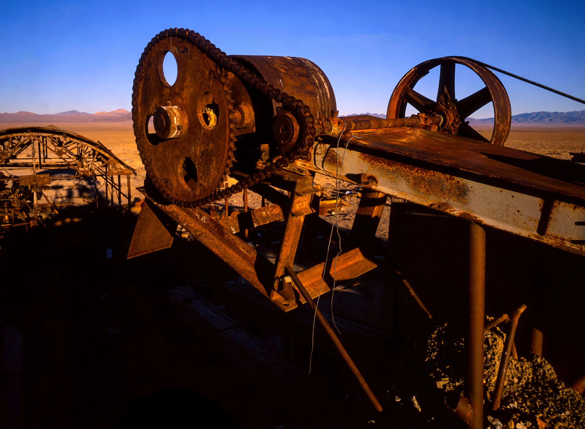 Rusted, abandoned mining machinery — a giant chain-driven gear and flywheel — weathering in the open desert near Rachel, Nevada