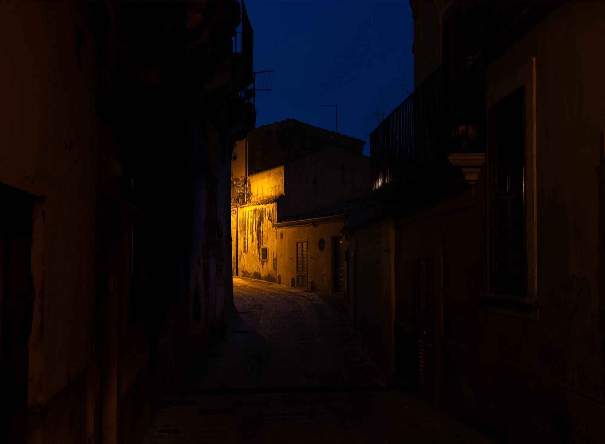 A dark alley in Ragusa Ibla at night, lit by a single streetlamp.