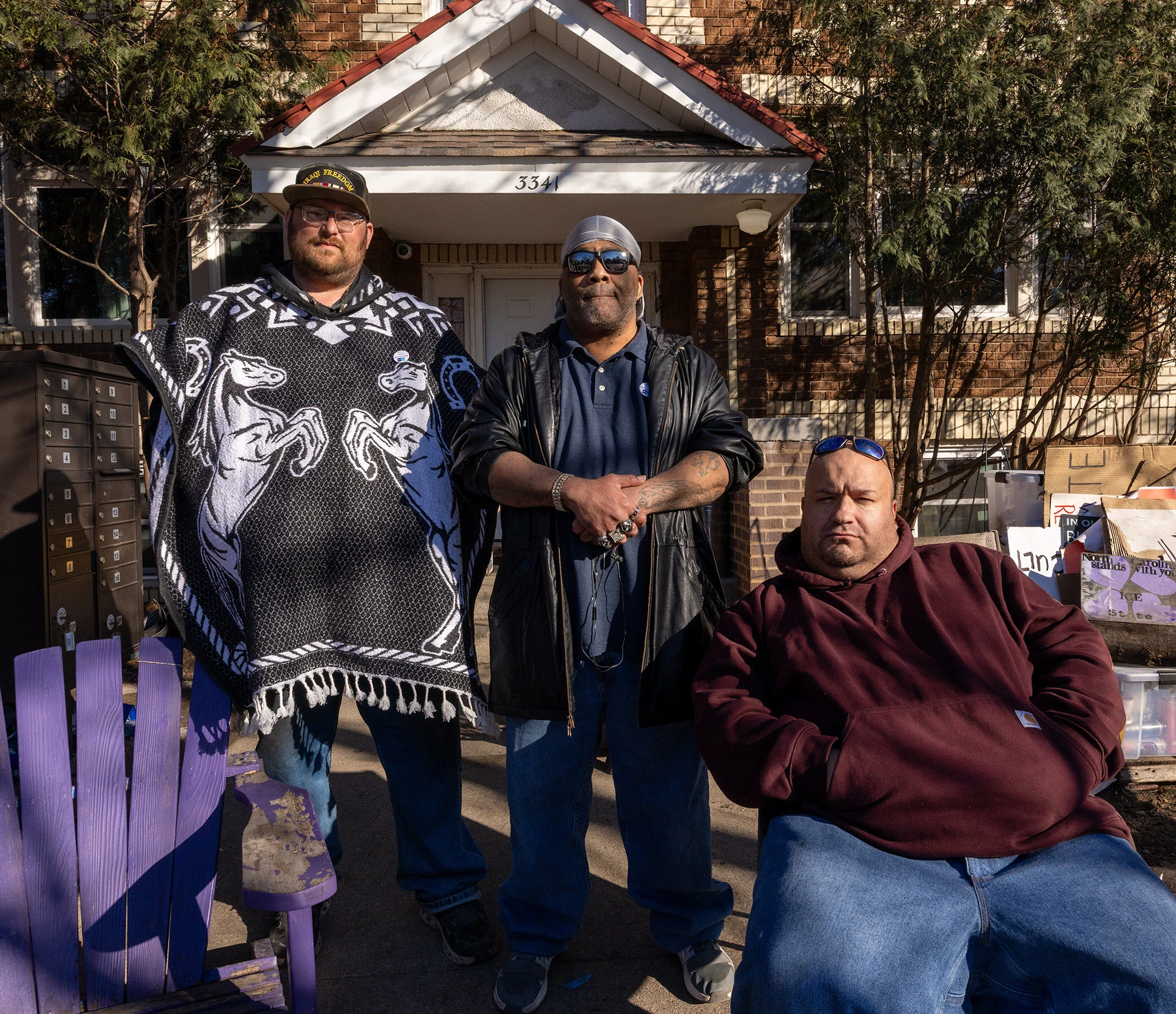 Three Minneapolis residents stand in front of the memorial for Renée Good, serving as everyday guardians of a makeshift shrine honoring her life after she was fatally shot by a federal ICE agent.