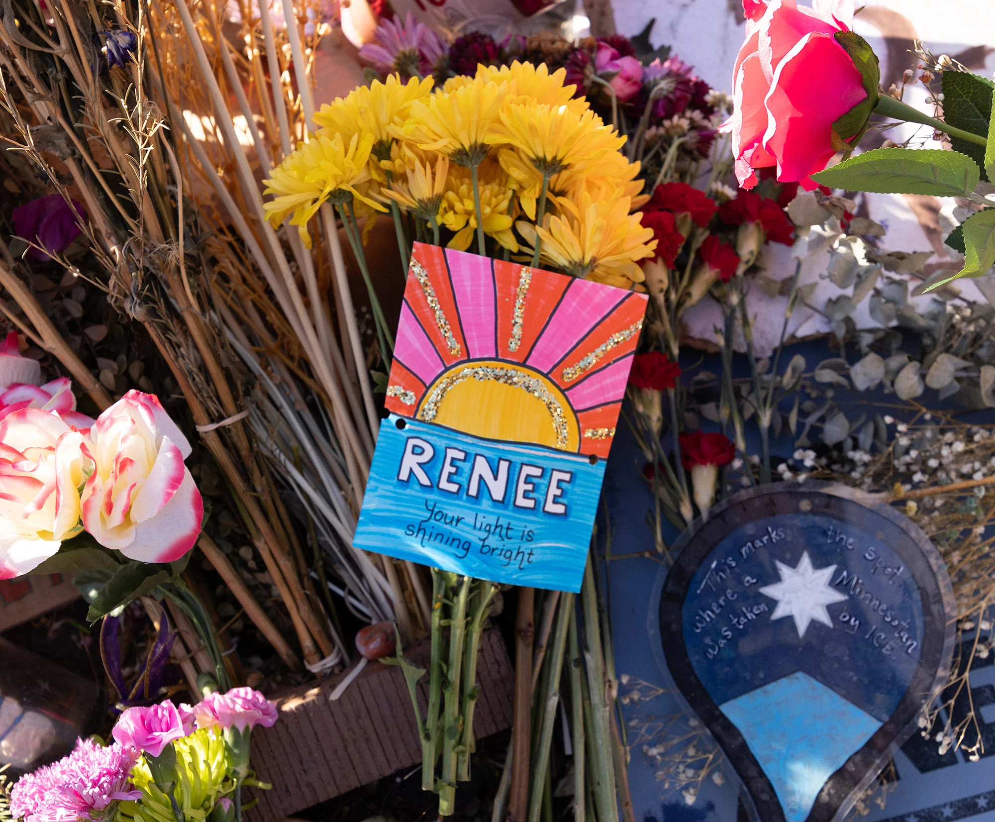 A handmade sign at the Renée Good memorial reads 'Renee — your light is shining bright,' placed among bouquets and flowers left by neighbors in Minneapolis after her death.